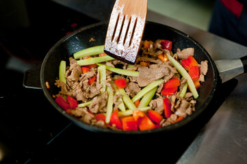 Cook fries meat in a pan with vegetables.