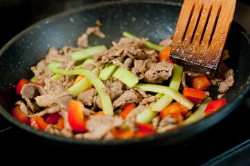 Cook fries meat in a pan with vegetables.