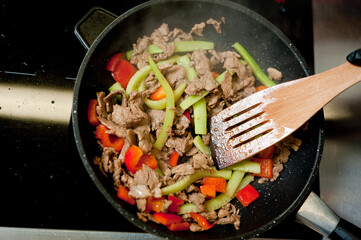 Cook fries meat in a pan with vegetables.