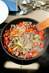 Cook fries meat in a pan with vegetables.