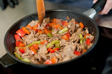 Cook fries meat in a pan with vegetables.