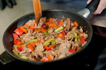 Cook fries meat in a pan with vegetables.