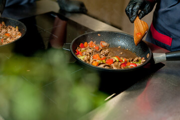 Cook fries meat in a pan with vegetables.