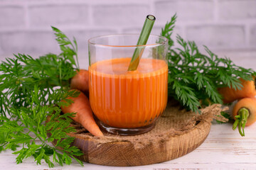 Carrot juice in a glass on a wooden tray.
