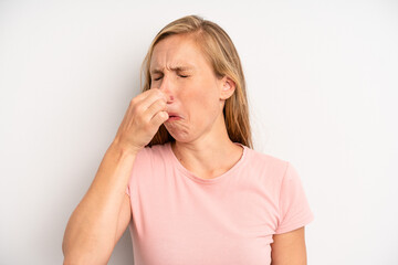 blonde pretty woman feeling disgusted, holding nose to avoid smelling a foul and unpleasant stench