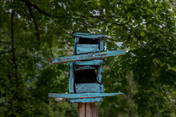 A very rough-made bird house or maybe a feeder on display in a yard in Woodstock in Upstate NY.  An abstractly built birdhouse is painted a bright blue but has faded over the years.