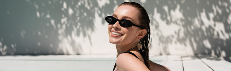 cheerful young woman with wet hair and stylish sunglasses sunbathing outside, banner.