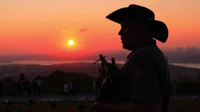 Silhouette man in a hat smoking a small cigar at an orange sunset in the evening