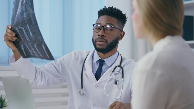 Male doctor looking at x-ray image, consulting patient on injury treatment