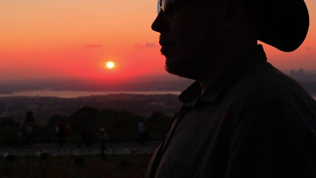 Silhouette man in a hat smoking a small cigar at an orange sunset in the evening