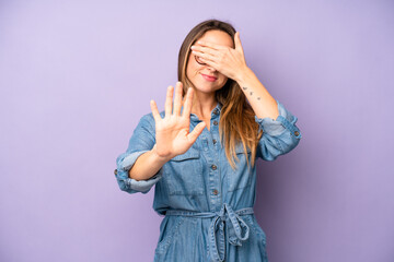 pretty young adult woman covering face with hand and putting other hand up front to stop camera,...