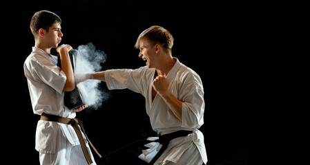 Dynamic portrait of male karate-do fighters in sports uniform training together isolated on black...