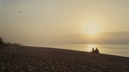 Young couple resting on beach at sunset. Wide shot lovers dating at ocean coast