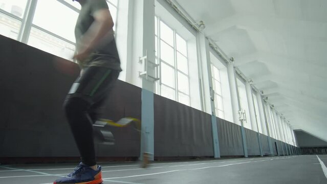 Sportsman putting on prosthetic running blade and then beginning run on track at indoor stadium