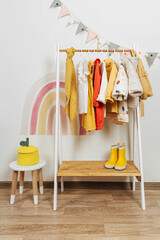 Wooden Clothing Rack with children's autumn outfits. Dresses, sweaters and jacket in kids room. Montessori wardrobe. Nursery Storage Ideas.
