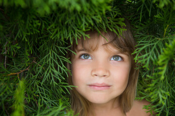 Relaxed child girl in thuja branches breathing fresh air with green branches in background. Aromatherapy and Spa concept. ecology. Earth Day. climate change