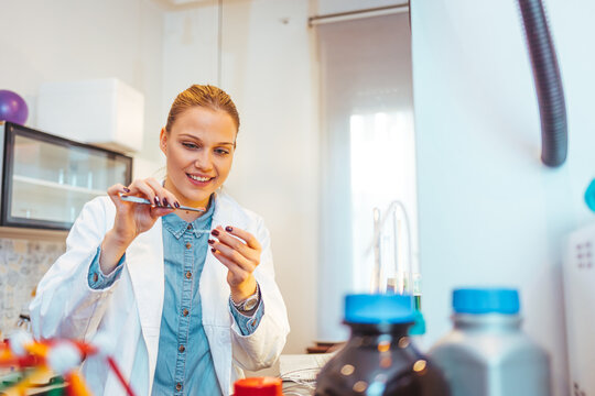 Female scientist working in the lab. A female medical or scientific researcher or woman doctor looking at a test tube of clear solution in a laboratory with her microscope beside her.