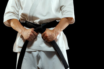 Cropped image of male karate fighter in white kimono and black belt in fighting stance on dark background. Sport, action, combat sports, ad concept © master1305