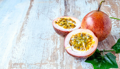 Fresh passion fruit and cut in half slice with green leaves isolated on wooden table background .