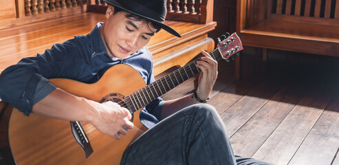 Asian male musician hipster playing acoustic guitar or practicing guitar for leisure or hobby hobby...