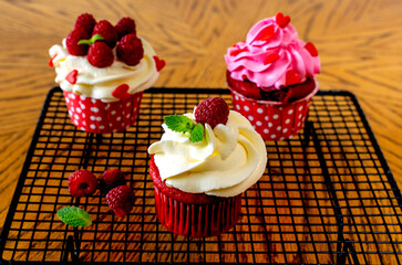 Red velvet cupcakes with cream, raspberries and mint, decorated with hearts. Preparation for the holiday. Sweet dessert. A confectionery stand stands on a wooden table.