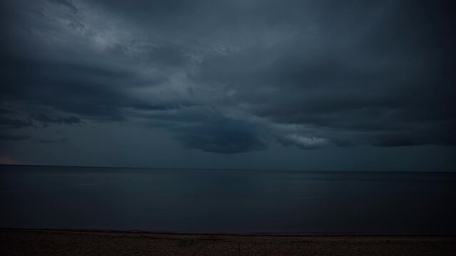 Static view of dark rain clouds passing by over the sea in timelapse along the empty sandy beach. Dark clouds float across the sky during evening time.