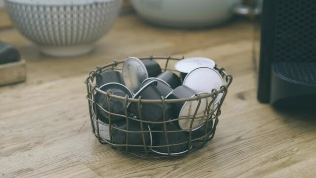 One hand takes a coffee pod from a container full of pods