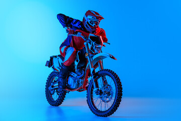 Portrait of young man, biker in full equipments riding motorbike isolated over blue studio...