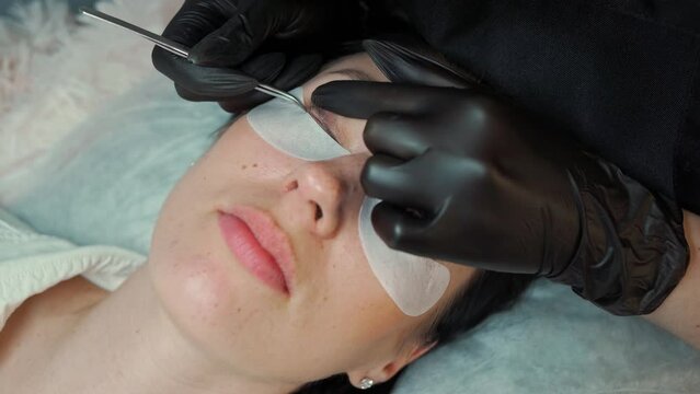 eyelash extension master in black gloves straightens eyelashes with a special spatula before extension. preparation for eyelash extensions