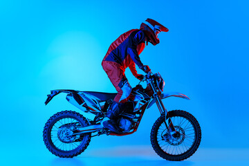Portrait of young man, biker standing on motorbike, riding isolated over blue studio background in neon light