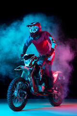 Portrait of young man, biker standing on motorbike isolated over dark background in neon light with...