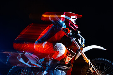 Portrait of young man, biker riding motorbike isolated over black background in neon with mixed...