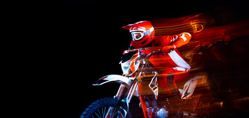 Portrait of young man, biker in full equipment riding motorbike isolated over black studio...