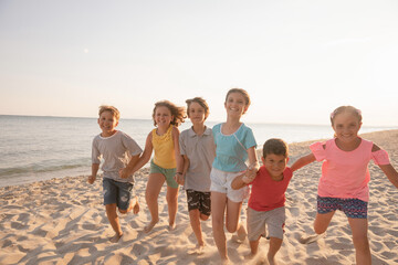 Happy kids running on the beach at sunset. Children having fun at summer holidays. Smiling boys and girls on vacation on seashore.