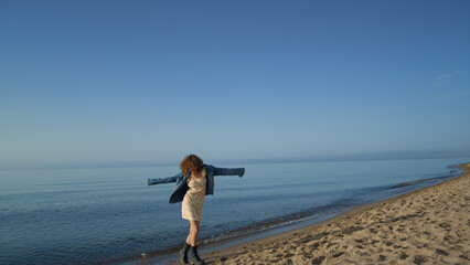 Fototapeta na wymiar Happy woman dancing at sea shore. Playful girl turning around on beach