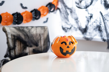 Plastic jack o lantern with marmalade on white table on halloween decorated background 