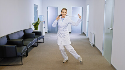 Beautiful young woman dancing charismatic in front of the camera enjoying the time in the modern hospital corridor