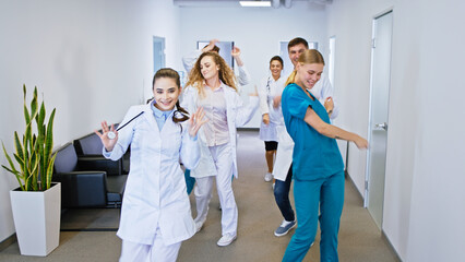Hospital stuff group of doctors and nurses in front of the camera dancing excited and looking straight to the camera they have large smile