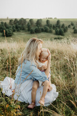 A young mother and little daughter hug and kiss on the field at sunset.