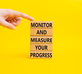 Monitor and Measure your Progress symbol. Wooden blocks with words Monitor and Measure your Progress. Beautiful yellow background. Businessman hand. Business concept. Copy space