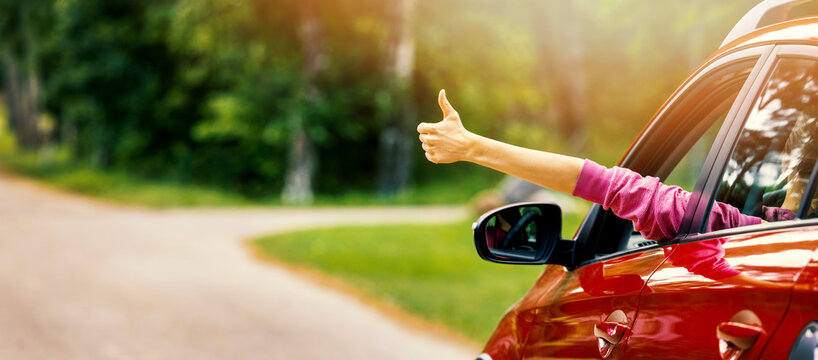 woman inside car on the road with thumb up gesture out of the window. banner with copy space