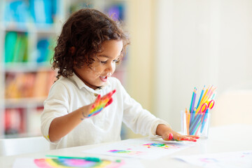 Child drawing rainbow. Paint on hands.