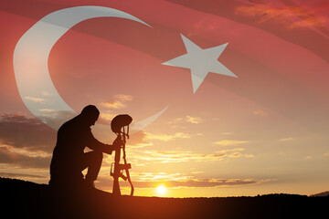 Silhouette of soldier kneeling with his head bowed against the sunrise or sunset and Turkey flag....