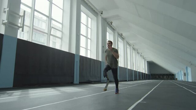 Slow motion shot of professional sportsman with prosthetic leg running on track while exercising at indoor stadium