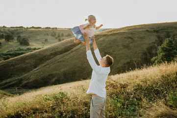 A young dad with a little daughter hugging, kissing and walking across the field at sunset.