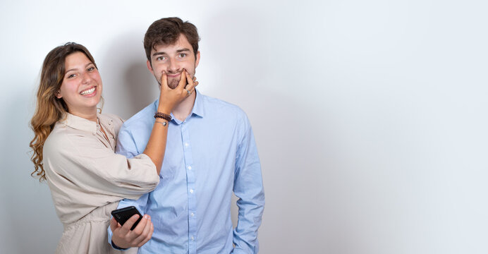 image fun et dr&ocirc;le d'un couple d'amis. La jeune femme fait sourire son ami avec sa main. Le jeune homme tient un t&eacute;l&eacute;phone dans sa main. Isol&eacute; sur fond blanc. Place libre pour le texte.