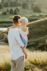 A young dad with a little daughter hugging, kissing and walking across the field at sunset.