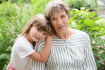 Fototapeta premium grandmother and little granddaughte hag and having fun together in the garden. Happy family enjoying summer outdoors.