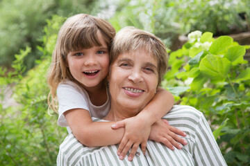 grandmother and little granddaughte hag and having fun together in the garden. Happy family enjoying summer outdoors.