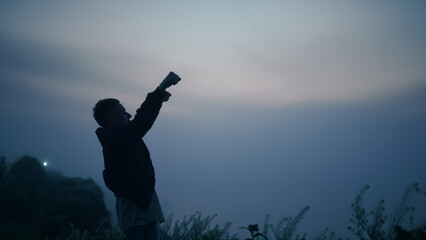 Guy standing on mountain edge at sunrise. Excited man raising hands in air
